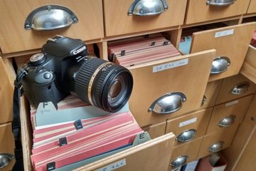 Auf einer mit Karteikarten gefüllten herausgezogenen Schublade ist eine moderne Digitalkamera positioniert.