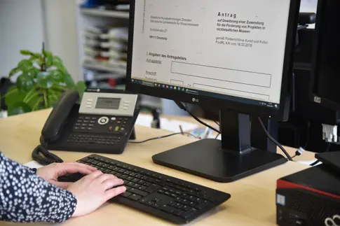 Schreibtisch mit Telefon und Computer, auf dem Bildschirm ein geöffnetes Antragsformular
