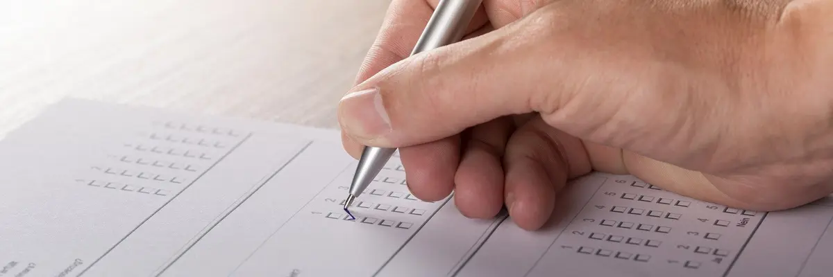 Nahaufnahme einer rechten Hand, die mit einem Kugelschreiber eine Fragebogen ausfüllt