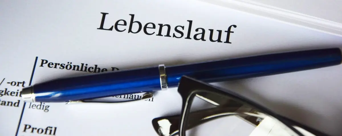 Nahaufnahme der Kopfzeile eines Lebenslaufes, darauf liegen ein Kugelschreiber und eine Brille.