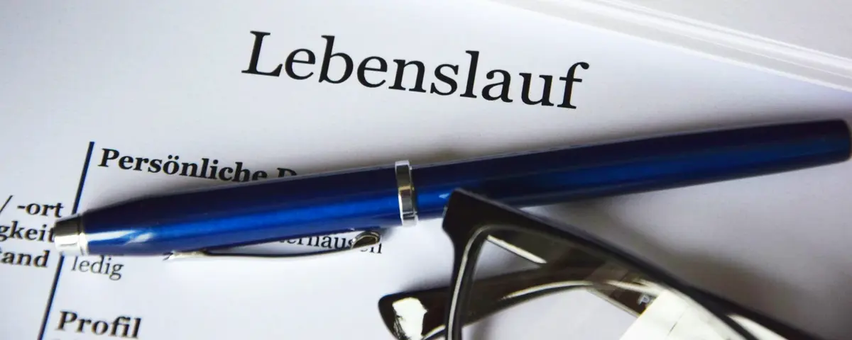 Nahaufnahme der Kopfzeile eines Lebenslaufes, darauf liegen ein Kugelschreiber und eine Brille.