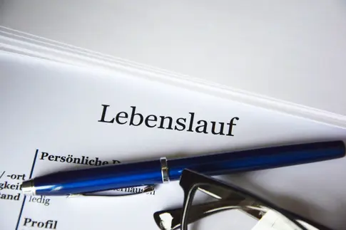 Nahaufnahme der Kopfzeile eines Lebenslaufes, darauf liegen ein Kugelschreiber und eine Brille.